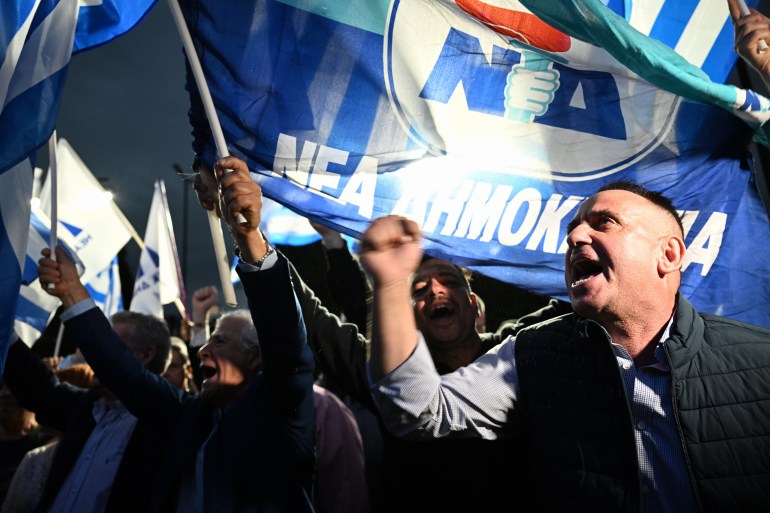 People wave the New Democracy's flag after the announcement of the first exit polls in front of the right wing party New Democracy's headquarters, in central Athens, on May 21, 2023. - The conservative party of Greece's outgoing Prime Minister holds a lead of up to 11 points in an election unlikely to produce a government, exit polls showed on may 21, 2023 (Photo by ARIS MESSINIS / AFP)