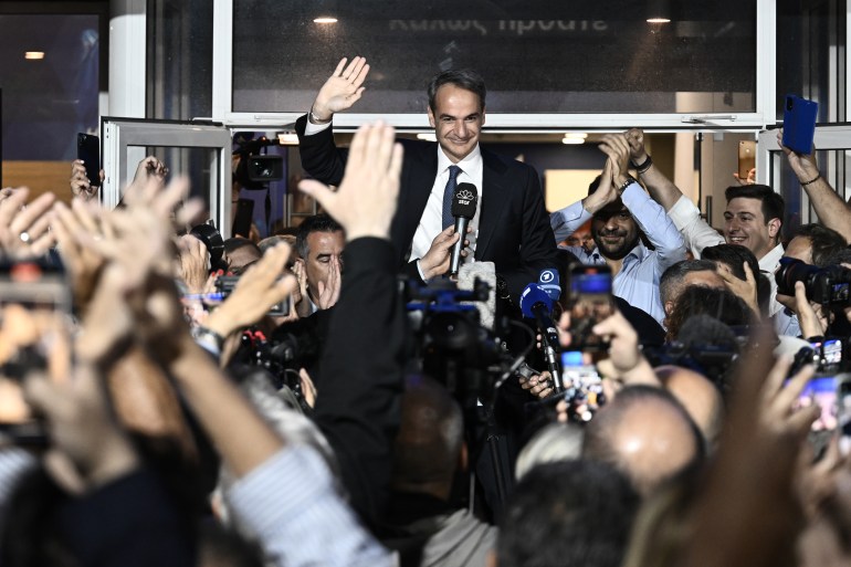 Prime Minister and New Democracy party's leader Kyriakos Mitsotakis celebrates with his supporters after his party's victory. He is waving and smiling.