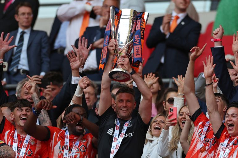 Luton Town's Welsh manager Rob Edwards lifts the trophy as Luton's players celebrate after they win the penalty shoot-out in the English Championship play-off final football match between Coventry City and Luton Town at Wembley Stadium in London on May 27, 2023. - Luton won the game 6-5 on penalties after the game finished 1-1 after extra time.