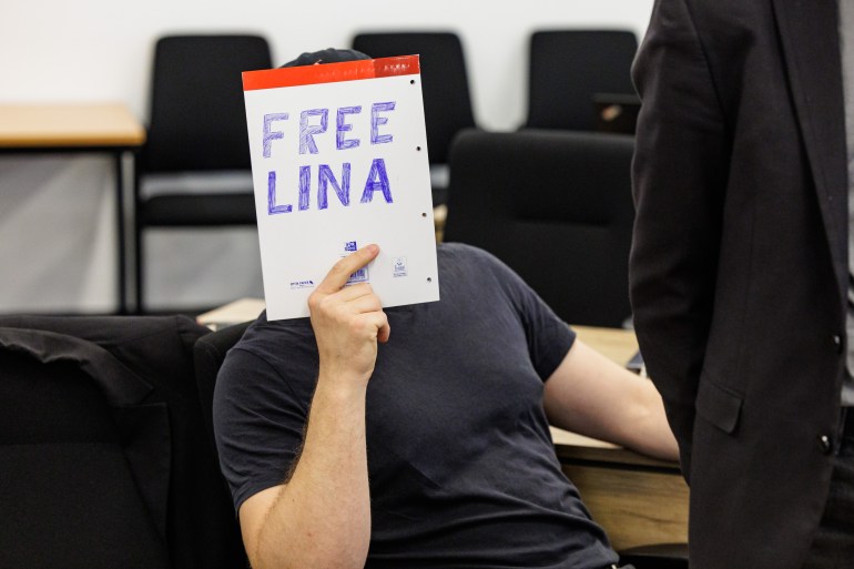 A defendant hides his face behind a sheet reading "Free Lina" as he sits the courtroom at the higher regional court in Dresden, eastern Germany, on May 31, 2023