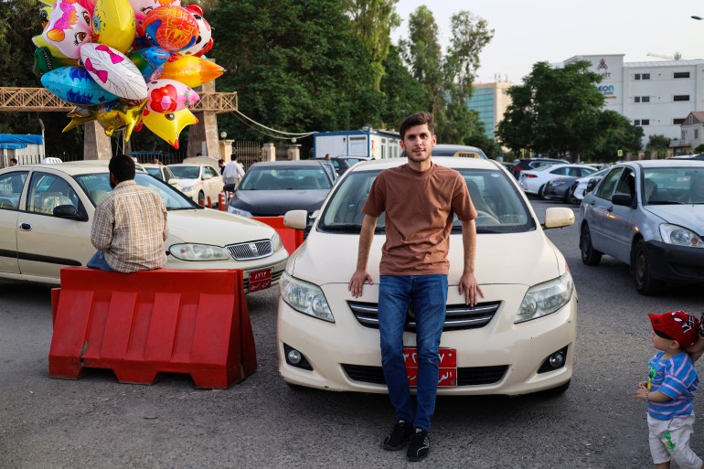 A photo of Mumen standing in front of his taxi by the entrance to Sami Abdulrahman Park.