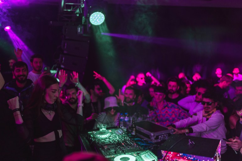 A photo of a group of people standing around a DJ.