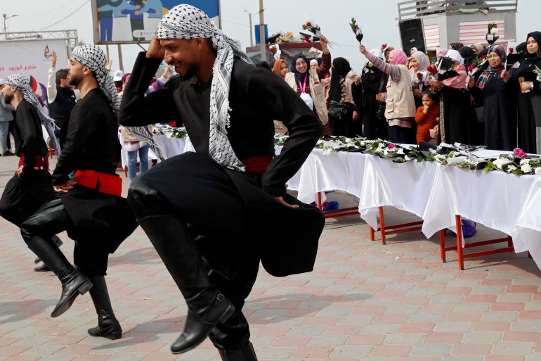 Men wearing traditional costumes perform Dabke, a Levantine folk dance seen at joyous occasions, in front of Palestinian women waving flowers while marking International Women's Day along the Mediterranean Sea in Gaza City, Tuesday, March 8, 2022. (AP Photo/Adel Hana)