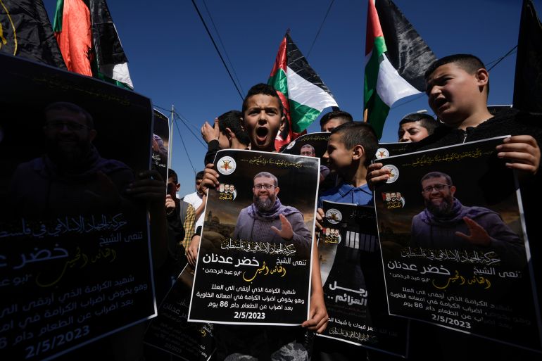 Palestinian kids wave their national flag and hold posters showing Khader Adnan