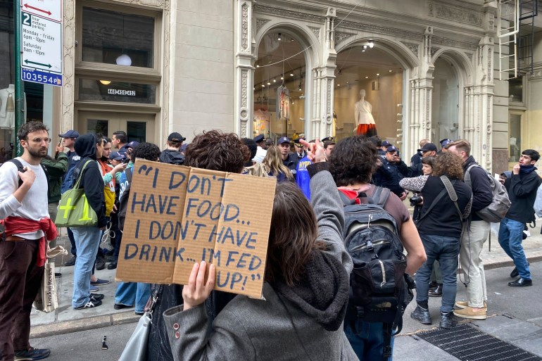 A woman holds up a cardboard sign reading: "I don't have food. I don't have drink. I'm fed up."