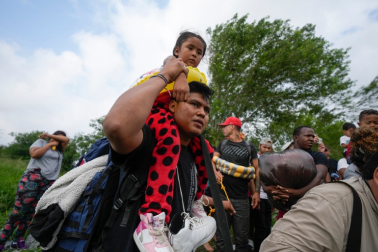 Migrant holding young girl on his shoulder as he walks amongst other people
