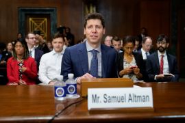 Sam Altman speaking at the Senate hearing. He is sitting at a wooden desk with his name in front. There are others seated behind him.