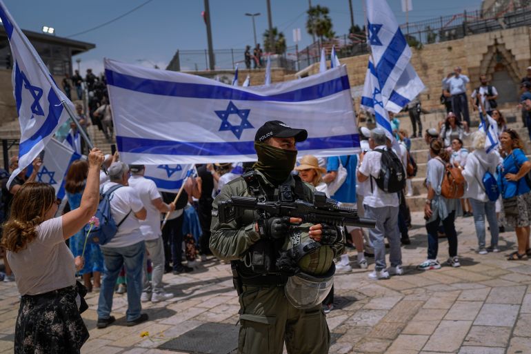 An Israeli police officer stands guard as Israelis wave national flags ahead of a march marking Jerusalem Day