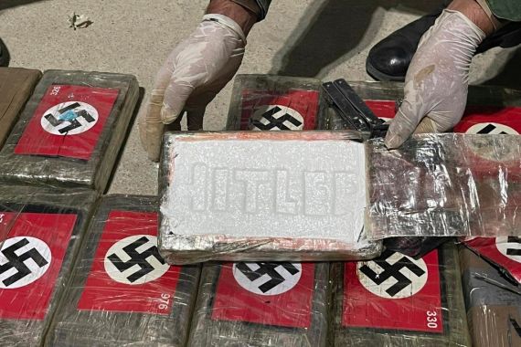 In this photo provided by the Peruvian Anti-Drug Police, an officer shows blocks of cocaine marked with Nazi swastikas and stamped with the name "HITLER", at the port of Paita, Piura region, Peru, Thursday, May 25, 2023. The police found more than 50 blocks of cocaine that were stashed in a container destined for a ship that was sailing for Belgium. (Peruvian Anti-Drug Police via AP)