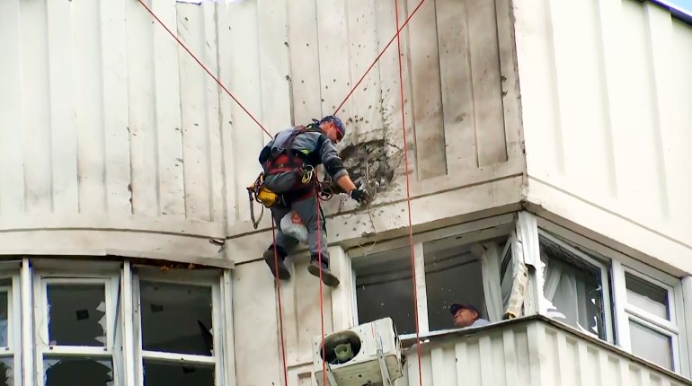 An investigator on a rope inspects the damage after a suspected Ukrainian drone hit a Moscow building. There is someone watching through the window from inside the building.