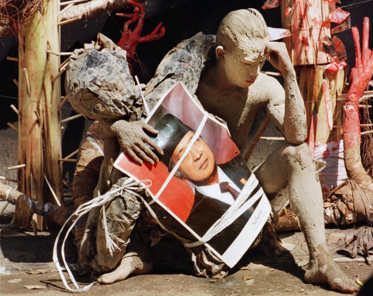 Covered in mud, a student shows his interpretation of former President Soeharto's fall from grace during a performance at Taman Ismail Marzuki Arts Center in Jakarta Wednesday, June 3, 1998. Student is holding a poster of Soeharto's portrait. [Muchtar Zakaria/AP]