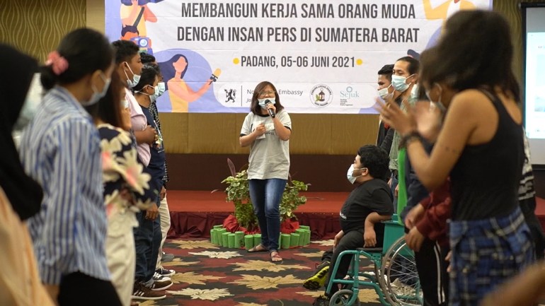 Angelique Maria Cuaca talking at an event. She is in the middle in front of the stage. There are lines of people on either side listening to her.