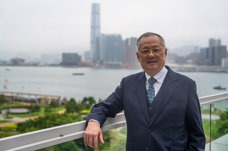 Tommy Cheung Yu-yan stands in front of a skyline view of Hong Kong. With his right arm resting on a railing, he looks at the camera with a slight smile.