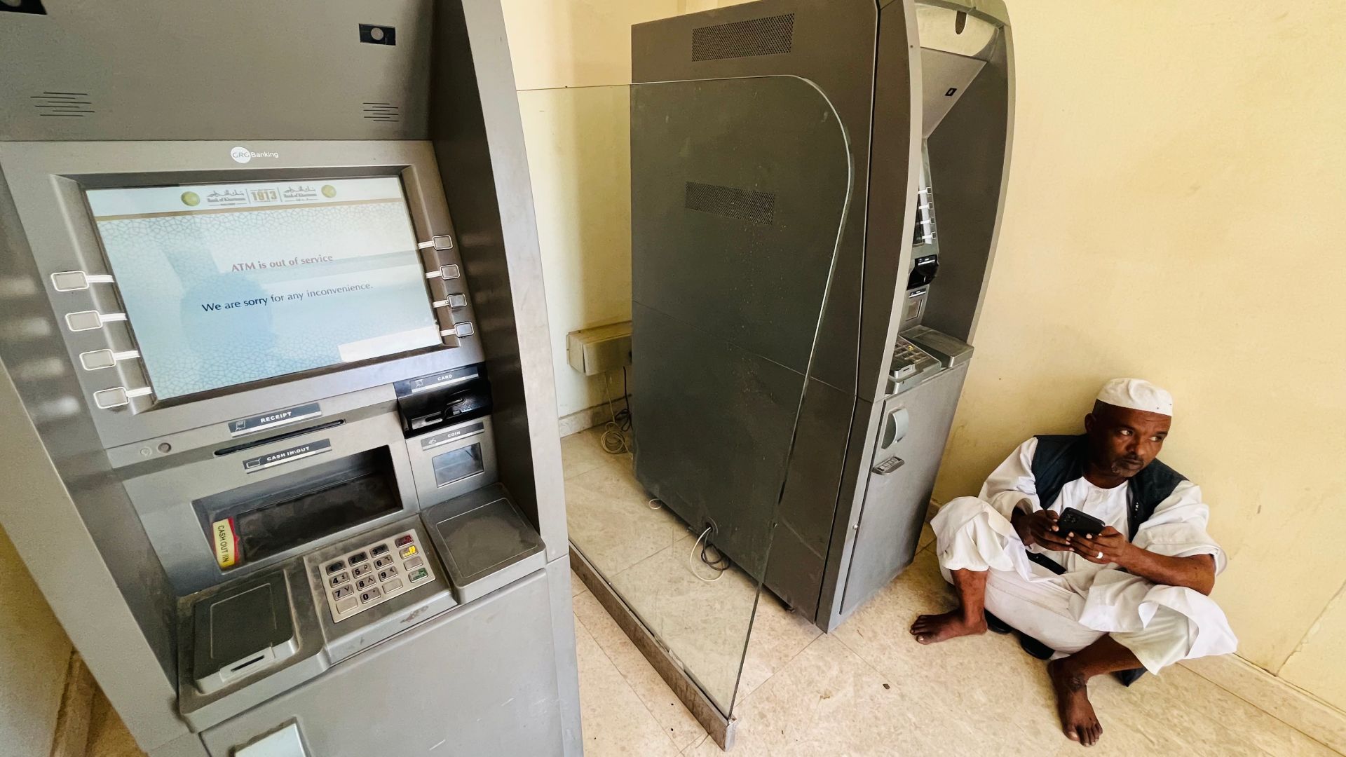 A man in Port Sudan sits exasperated near an out of service ATM