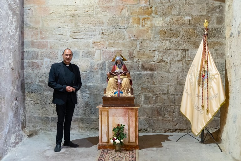 Father Antonio Rosario poses in the Old Church of Saint Michael next to a copy of the Holy Trinity.