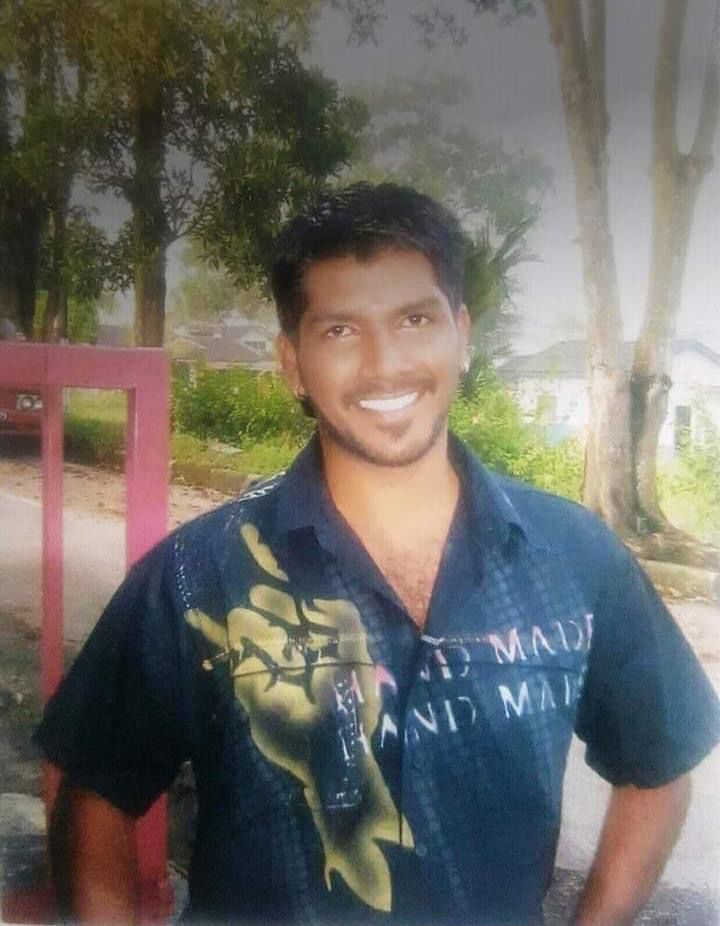 Datchinamurthy posing for a photo. He's standing outside, smiling and has his hands on his hips. He's wearing a black short-sleeved shirt