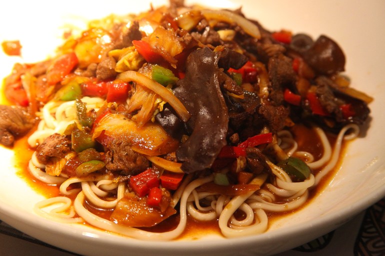A close-up of a white plate with a noodles, onions, peppers and mushrooms on top.