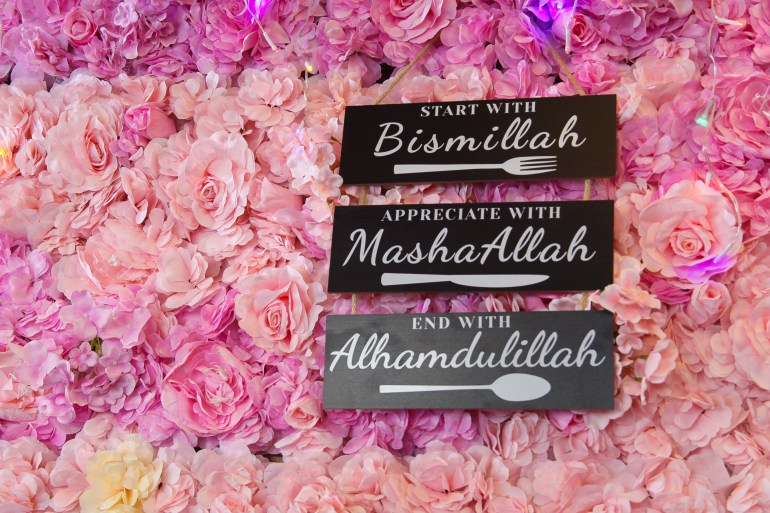 Three signs sit against a wall of pink roses. They read: "Start with Bismillah. Appreciate with MashaAllah. End with Alhamdulillah."