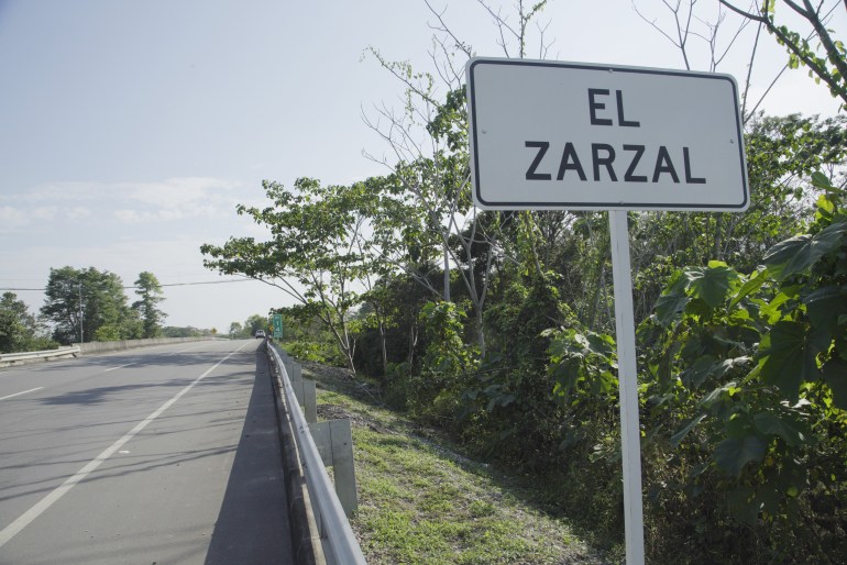 A roadside sign reads "El Zarzal." To the side, bushes and greenery can be seen.