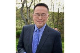 Tan Twan Eng wearing a suit with a blue shirt and tie. He is standing outside in a garden, and smiling.