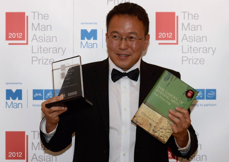 Tan Twan Eng holding the Man Asian Literary Prize after winning the 2012 award. He looks very happy. He is also holding the book in one hand. 