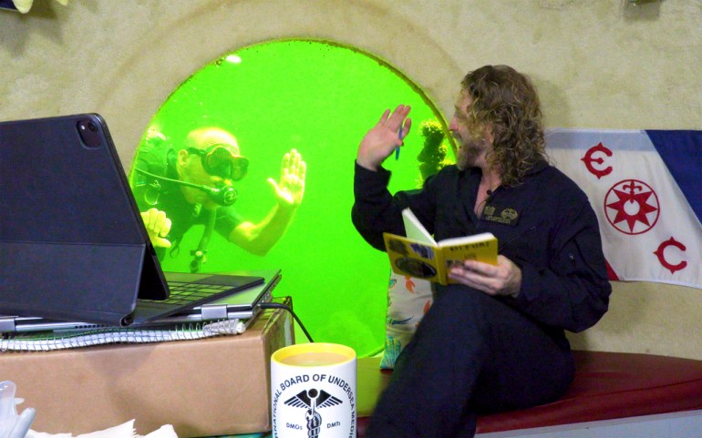Researcher waves to a scuba diver from his window