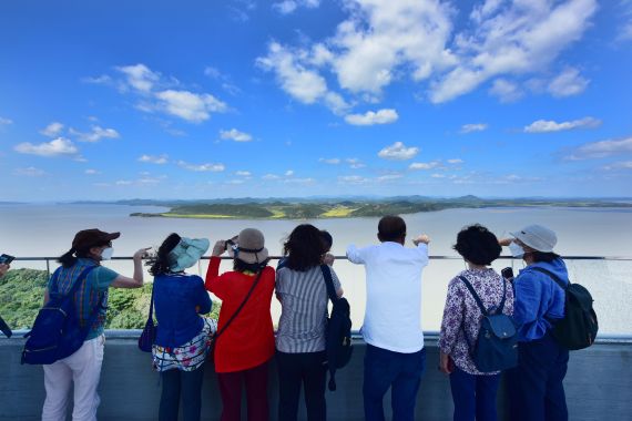 A group of Korean tourists look out at North Korea from the Gimpo-Aegibong Observatory. They have their backs to the camera.