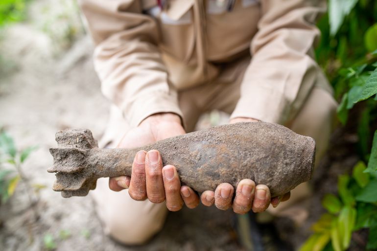 A close up of an unexploded bomb discovered in Vietnam. An explosives expert is holding it. It has mud on it