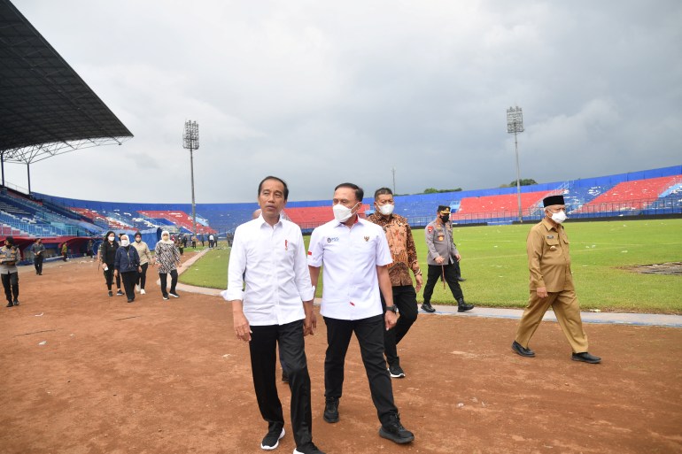 Indonesian President Joko Widodo visiting the stadium after the the tragedy. He is walking with the Chairman of the Indonesian Football Association on the path around the pitch. He is wearing is trademark white shirt, black trousers and black trainers.