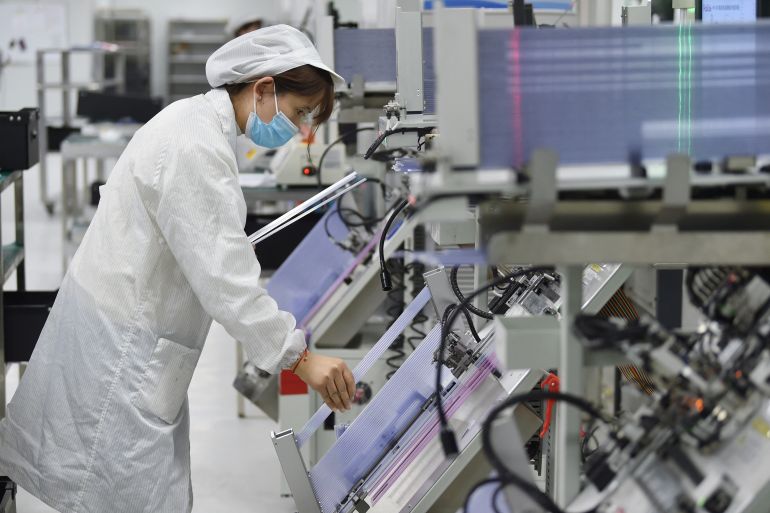 An employee working on a semiconductor production line in China. They are wearing a white coat and hairnet.