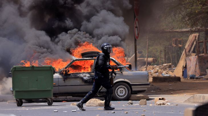 A riot police officer walks near a car set on fire during clashes between supporters of Senegalese opposition leader Ousmane Sonko and security forces after Sonko was sentenced to prison in Dakar