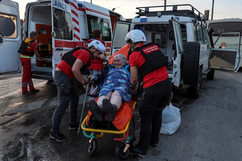 Red Cross volunteers help an elderly woman evacuated from a flooded area after the Nova Kakhovka dam breached, amid Russia's attack on Ukraine, in Kherson, Ukraine