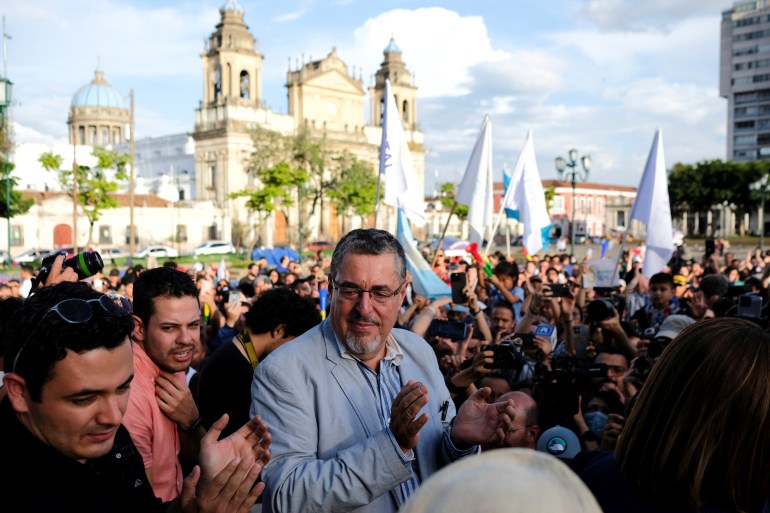 A man in a light-blue suit walks through Guatemala City's central square, surrounded by well-wishers.