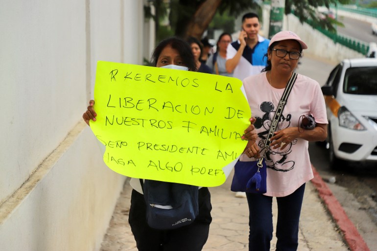A woman holds a yellow poster, calling for the liberation of her family member as she walks through the street.