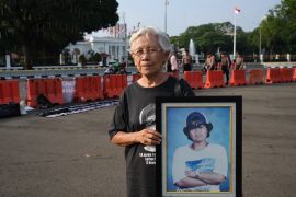 Maria Catarina Sumarsih holds a picture of her son who was shot dead in 1998 during the student protests. The Presidential Palace is behind her with the Indonesian flag flying. There are police standing behind plastic barricades