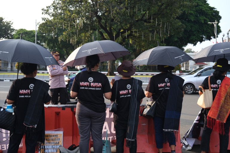 Demonstrators standing beneath black umbrellas. They are on the road opposite the presidential palace in Jakarta. They are wearing T-shirts reading 'dark dreams' on the back
