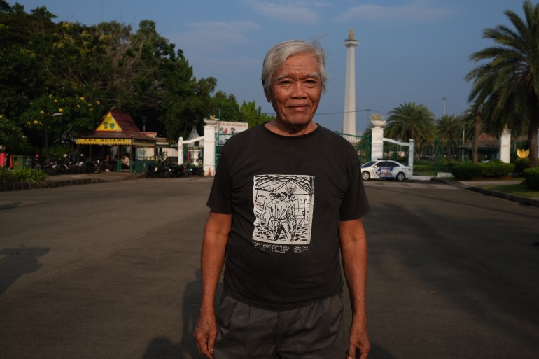 Bejo Untung standing in Jakarta. He is wearing a black T-shirt. MONAS, the national monument, is behind him. 