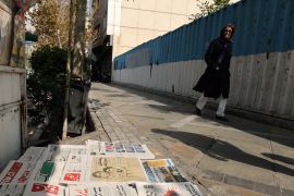 A woman walks past a kiosque in the Iranian capital Tehran on October 30, 2022, displaying copies of the Hammihan newspaper, featuring on its cover a headline mentioning the statement by the Tehran journalists' association, criticising the detention by authorities of two journalists, Niloufar Hamedi and Elaheh Mohammadi (drawing on cover), who according to local media, helped publicise the case of Masha Amini