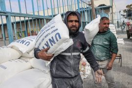 Palestinians carry bags of flour destined for poor families at the United Nations Relief and Works Agency for Palestine Refugees (UNRWA) distribution centre, in Rafah refugee camp in the southern Gaza Strip, on January 22, 2023 [Said Khatib/AFP]