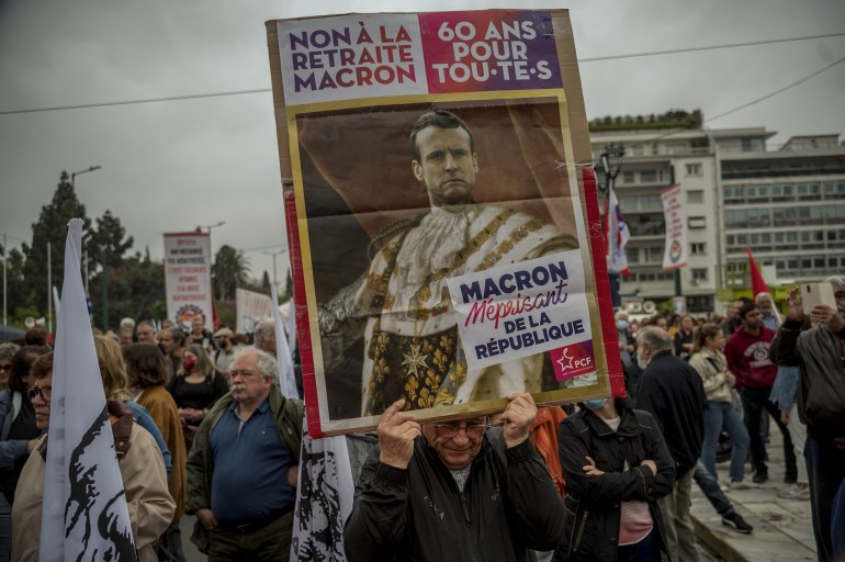 A man from French Communist Party (PCF) holds a placard depicting French President disguished as a King and reading "No to the Macron's pension, 60-year-old for everyone, Macron disdainful of French Republic", as he protests during the May Day celebrations, to mark the international day of the worker, in central Athens on May 1, 2023. (Photo by Angelos Tzortzinis / AFP)