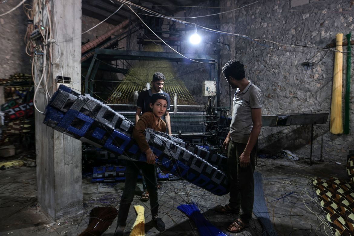 In this picture taken on June 1, 2023, a child and men work at a factory making mats and rugs