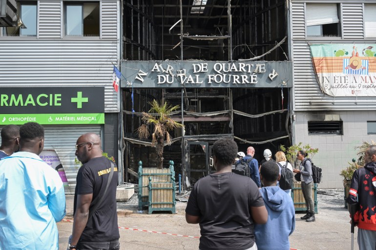 Local residents look on next to the facade of a burnt-down annex town hall of the Le Val Fouree neighbourhood in Mantes-la-Joli