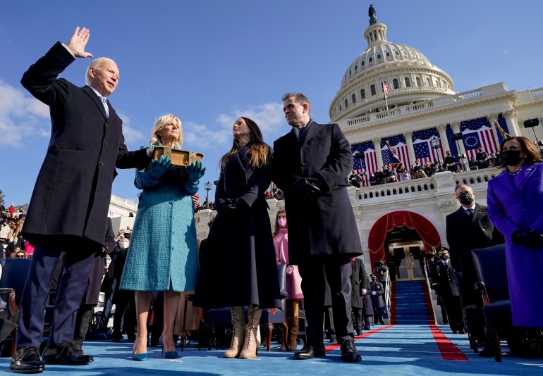 A man raises his right hand and places another on a book on the steps of the Capitol to be sworn in as president. His family looks on.