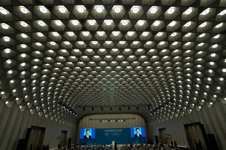 A view of the hall for the forum titled Chinese Modernization and the World. There are two large screens showing a formal portrait of Xi Jinping