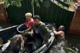 Residents and their dog are evacuated on a boat from a flooded neighbourhood in Kherson, Ukraine [Libkos/AP]