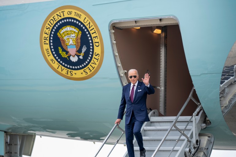 A man in aviator sunglasses waves and descends the steps of a baby-blue airplane, emblazoned with the presidential seal.