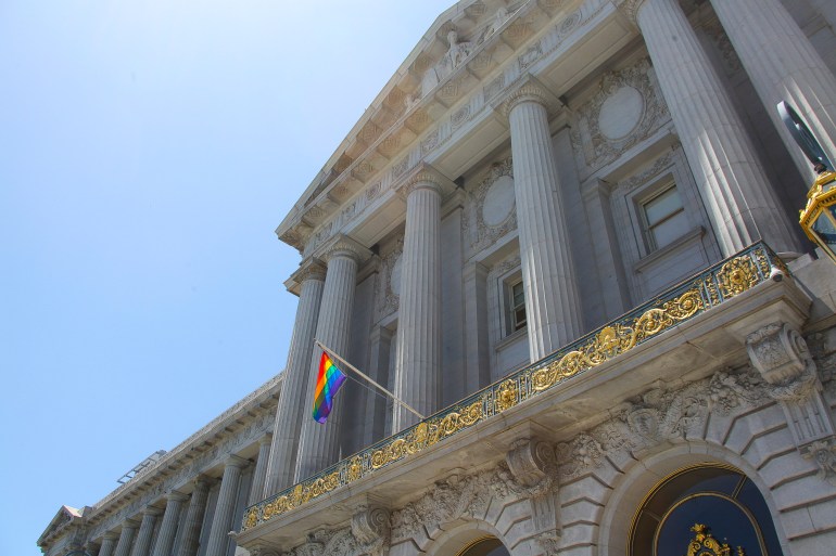 A rainbow flag waves from an ornate balustrade at San Francisco's city hall.