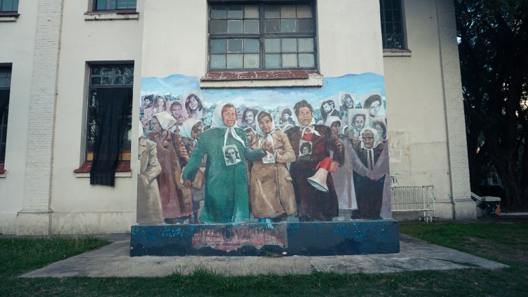 A mural depicts women in white head scarves carrying photos of their loved ones.