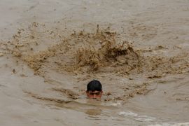 A man swims in floodwaters while heading for higher ground [File: Fayaz Aziz/Reuters]