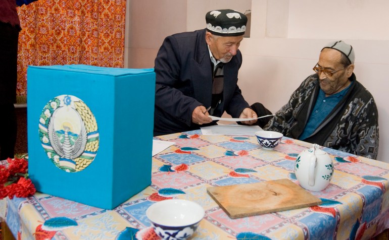A visiting member of a local election committee (L) shows a ballot to a man at his home during a parliamentary election in Tashkent